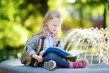 Adorable little schoolgirl in a city park on bright autumn day