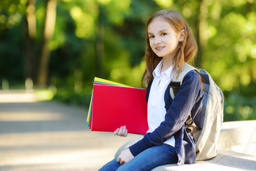 Fototapeta premium Adorable little schoolgirl in a city park on bright autumn day