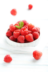 Red raspberries in bowl on a white wooden table
