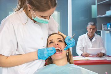 Young woman on medical exam at dentist office. Dentist in the background.