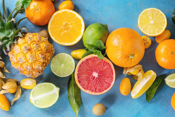 Fototapeta na wymiar Variety of whole and sliced citrus fruits pineapple, grapefruit, lemon, lime, kumquat, clementine and physalis with mint over blue wooden background. Top view with space. Healthy eating, dieting