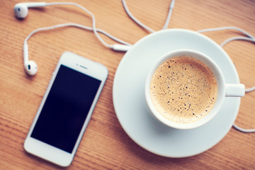 Smartphone, headphones and coffee cup on wooden table