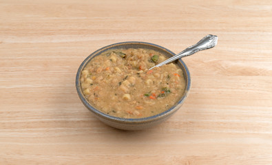 White bean soup in a bowl with a spoon atop a wood table.