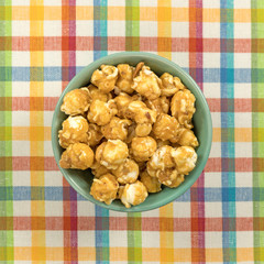 Toffee caramel popcorn in a green bowl atop a colorful place mat.