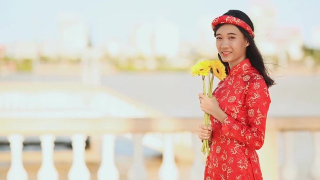 Beautiful Vietnamese girl in red traditional dress Ao Dai with yellow flowers.