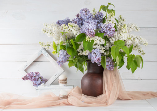 Lilac bouquet in clay jug with photo frame and candles