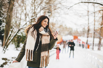 Young woman using a phone in the winter park