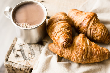 Freshly baked croissants on linen cloth, aluminum mug with hot cocoa on vintage wood box, cozy atmosphere, kinfolk