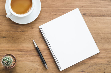 Wooden desk table with notebook, pen, cactus and cup of coffee.