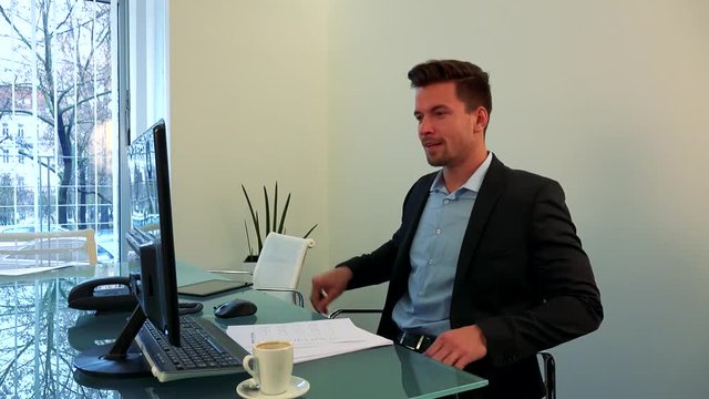 A young, handsome man sits down to a table in his office and works on a computer
