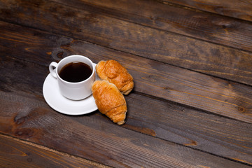White mug of coffee and a croissant on a wooden background