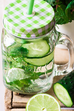 Mason Jar Mug With Handle, Lid And Straw With Detox Cucumber Agua Fresca Water With Lime And Mint Ingredients, On Vintage Plank Wood, Outdoors, Spring Cleansing