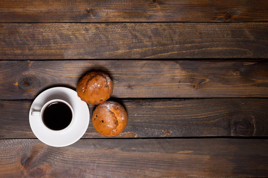White mug of coffee and two cupcakes on wooden background