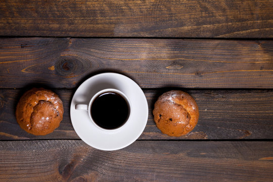 White mug of coffee and two cupcakes on wooden background