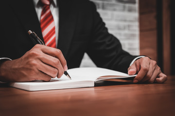 Fototapeta na wymiar Businessman in suit writing or signing in notebook on wooden tab