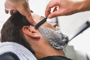 Skillful hairdresser shaving beard by blade