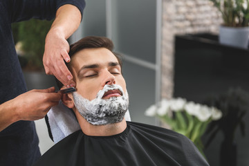 Professional hairdresser shaving beard of customer