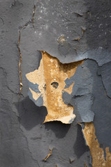 Part of the wall with cracked gray paint that is peeling off. The second layer of the wall is painted in yellow color