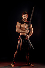 Portrait of handsome muscular gladiator with sword. Studio shot. Black background.
