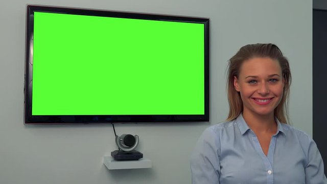 A young, beautiful woman smiles at the camera, a green television screen in the background
