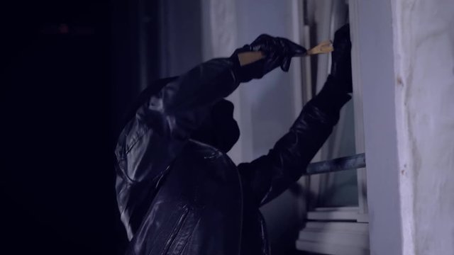 Einbrecher mit Brecheisen und Taschenlampe vor Fenster