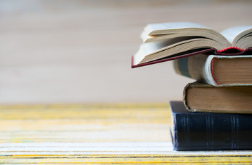 Open book, stack of hardback books on wooden table.