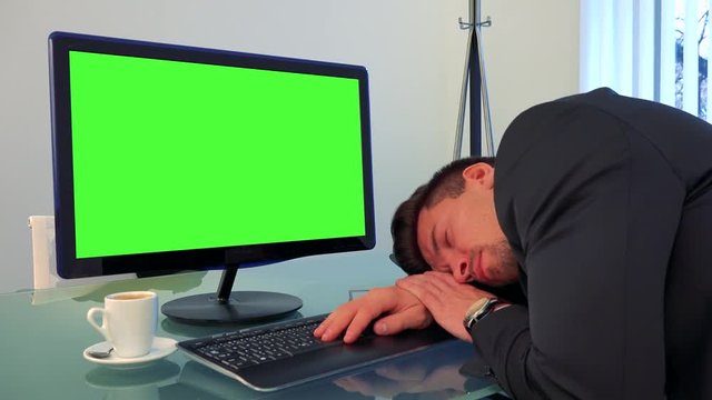 A young, handsome man sleeps on a desk in front of a green computer screen