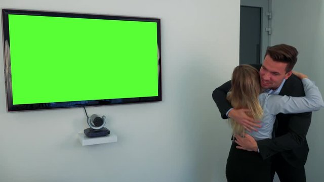 A man and a woman celebrate in front of a green television screen
