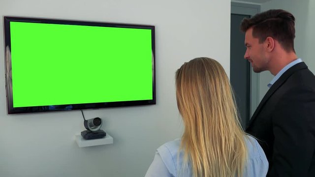 A man and a woman talk to a green television screen