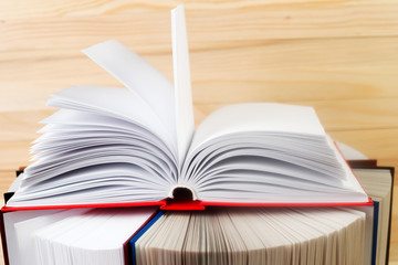 Open book, stack of hardback books on wooden table.