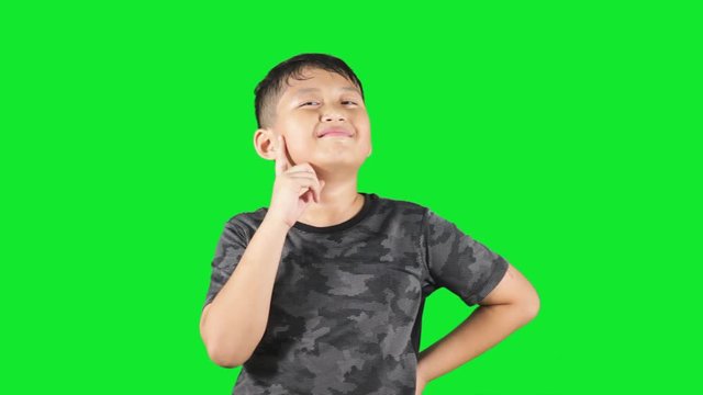 Cute boy standing in the studio while thinking idea and looks get an idea, shot with green background