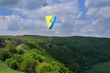 Paraglider with a paramotor flies over the river valley in summer sunny day. Dniester river, Ukraine.