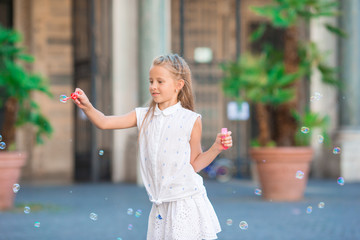 Adorable little girl blowing soap bubbles in european city. Portrait of caucasian kid enjoy summer...