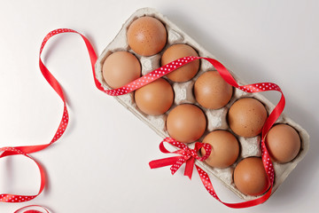 Raw brown eggs in an egg carton with red polka dot ribbon and bow on white background. Top view