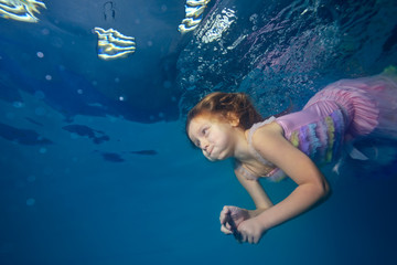 Fototapeta na wymiar Child, the little girl dives under the water in a beautiful dress on a blue background. Portrait. Close-up. Shooting under the water surface. Horizontal view