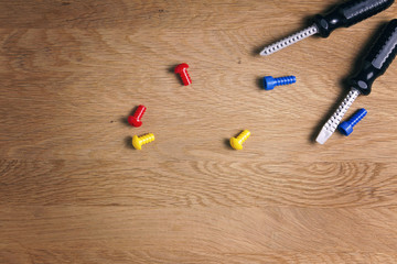 Kids construction toys tools: colorful screwdrivers, screws and nuts on wooden background. Top view. Flat lay. Copy space for text