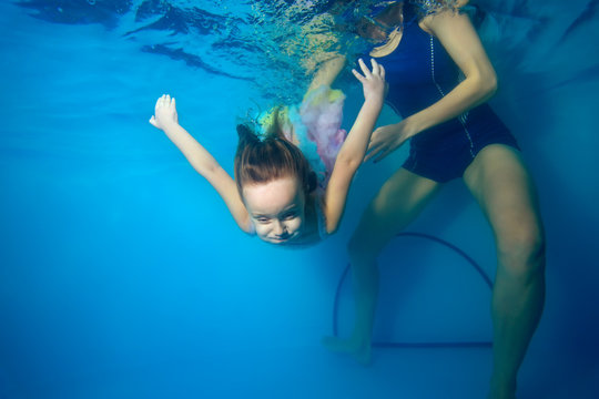 The child is involved in sports with a coach in the pool and dives under the water. Portrait. The view from under the water. Landscape orientation