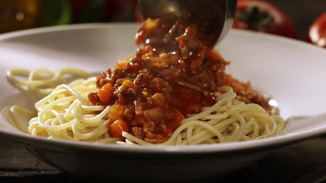 Spooning tasty Bolognaise or Bolognese sauce onto a plateful of cooked Italian spaghetti from a metal ladle in a close up view