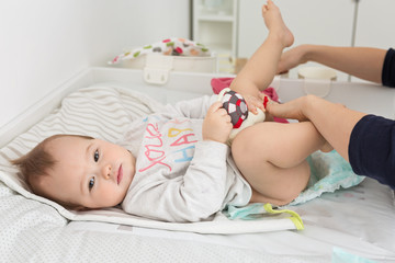 Mother changing diapers of a nine months old baby girl daughter;