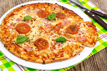 Pizza with ham, cheese, tomatoes and basil