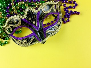 Mardi gras mask and beads on a yellow background with copy space