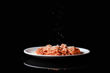 Pasta spaghetti macaroni with parmesan cheese on white plate on black background.