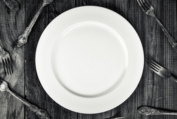 White empty plate among forks, top view