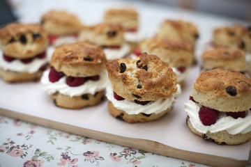 Fruit scones with cream and raspberries on a wooden board on a floral tablecloth
