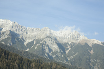 Fototapeta premium Austria, Tyrol, Alps - 3 January 2017 A light cloud floating over the mountain ranges of the Alps which are covered with snow and forests.