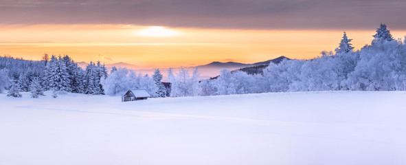 Panorama of an idyllic white winter landscape with a little wooden hut in background