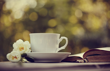 Old open book and a white cup with a wild roses