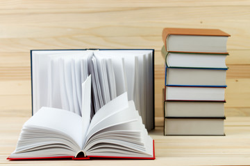 Open book, stack of hardback books on wooden table.