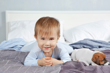 Cute little boy with funny puppy on bed at home