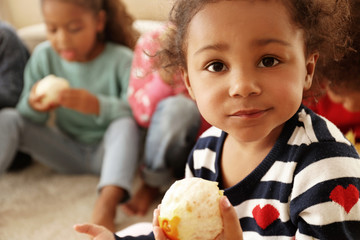 Fototapeta premium Cute African girls sitting on floor and eating orange